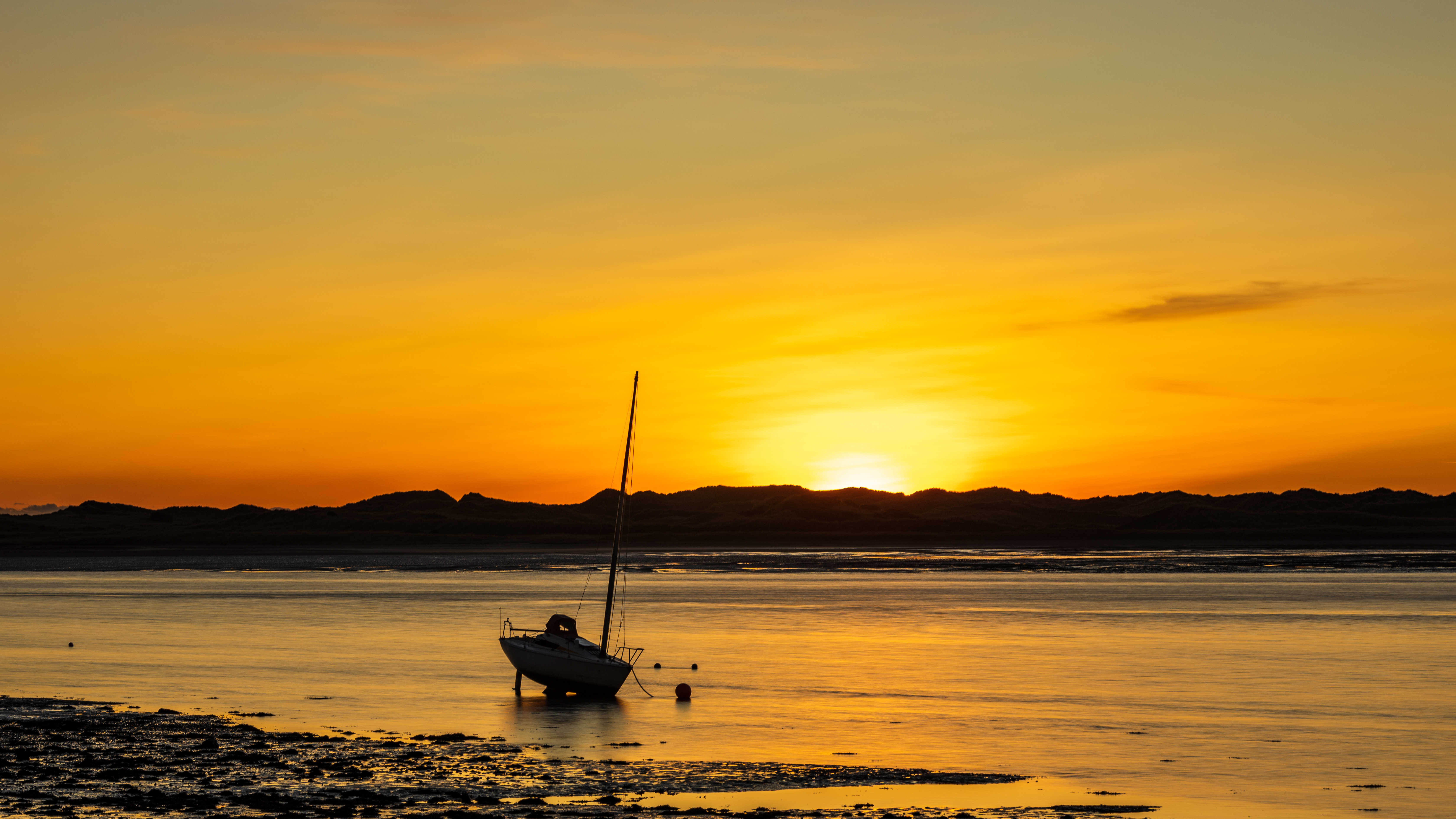 Sunset at Ravenglass beach, with the last rays of sunshine shedding light over the sea and one singular boat resting on the shoreline